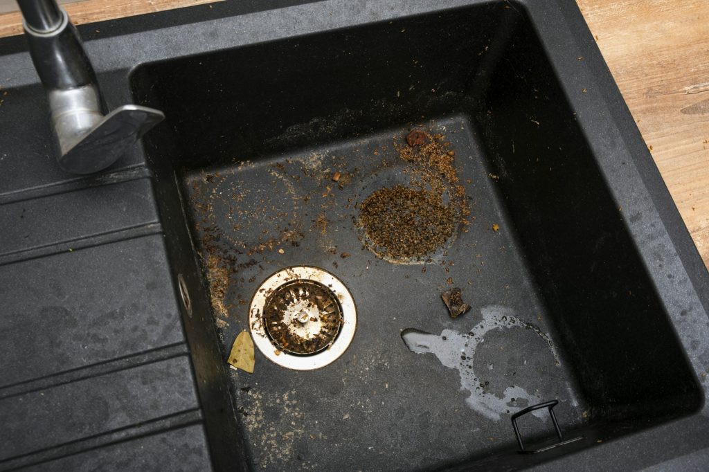 Dirty granite kitchen sink black with leftover bits of food. Before. House cleaning service