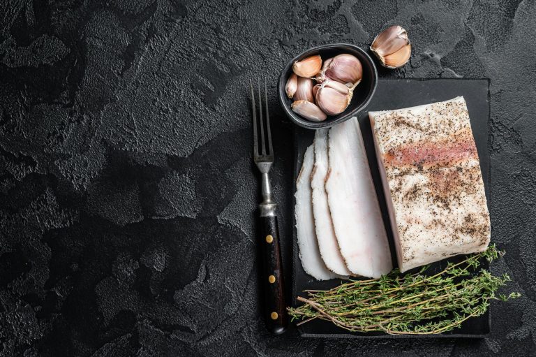 Sliced Salty lard with garlic and black pepper on marble board. Black background.